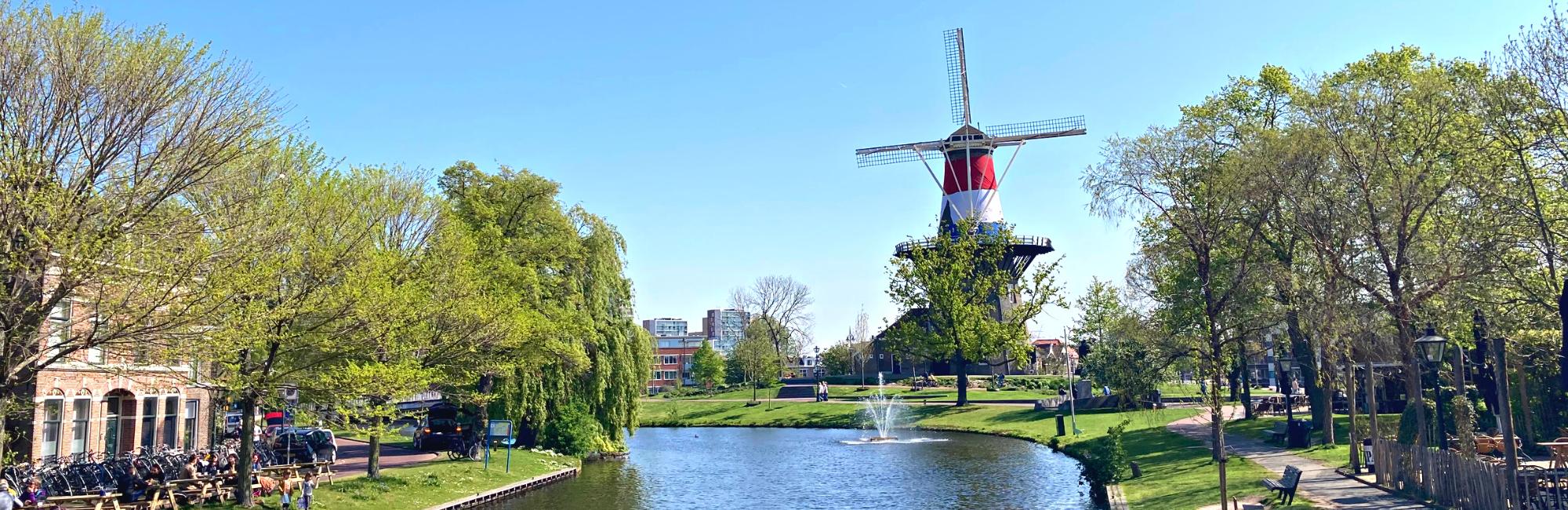 Canale con una fontana sulla destra e un mulino con la bandiera dei Paesi Bassi in fondo