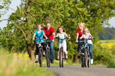 Una famiglia felice, con 3 bambini, stanno pedalando in una prateria olandese del sud dell'Olanda. Dietro a loro un albero con foglie verdi
