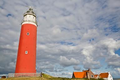 Un cielo coperto di nuvole grigie e il faro rosso e bianco di Texel, la casetta di guardia è sullo sfondo 