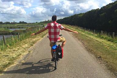 Rgazzo con una camicia a scacchi rossi e bianchi, sta pedalando senza mani lungo la pista ciclabile, in direzione Zandvoort
