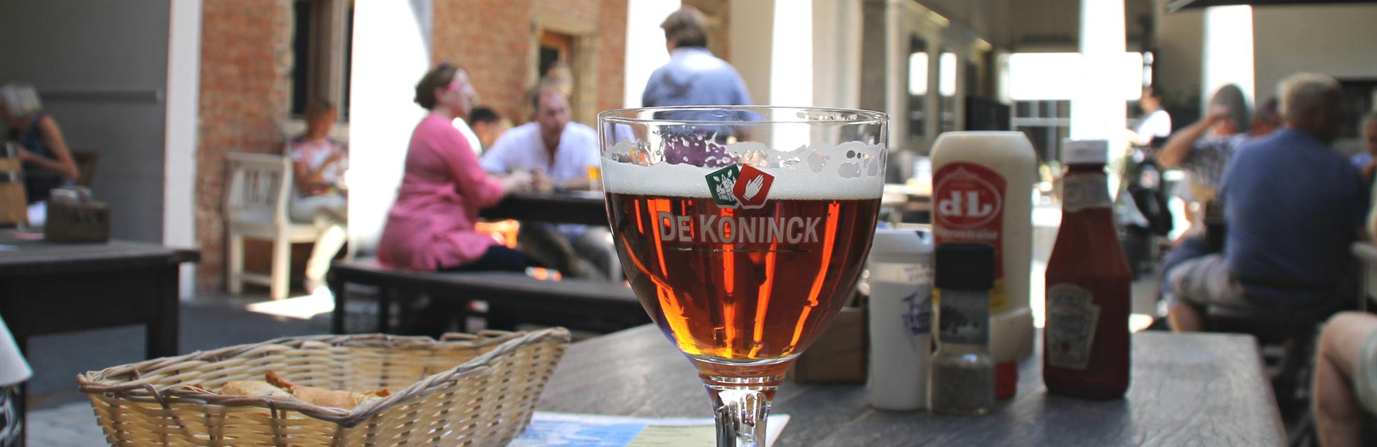 Birra nel bicchiere De Koninck, in un bar con altre persone