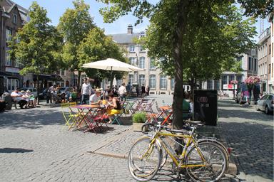 Biciclette appoggiate ad un albero e persone sedute su tavolini colorati e un tendone bianco li copre dall'ombra