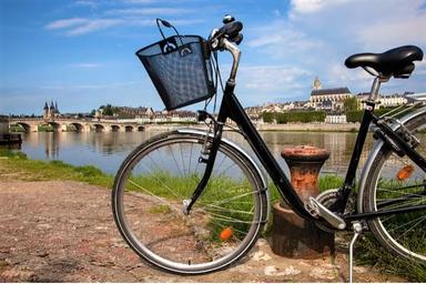 In primo piano una bicicletta nera con cavalletto, sull'argine della Loira, in lontananza un ponte
