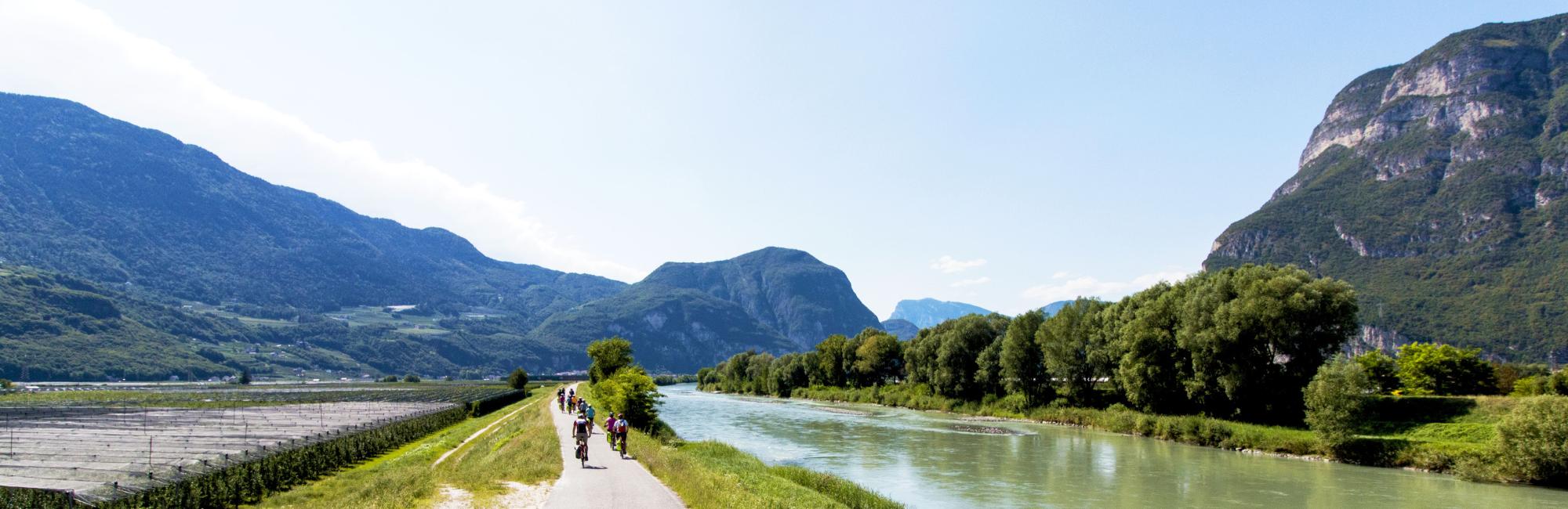 Persone che pedalano in una valle circondata da montagne e un fiume