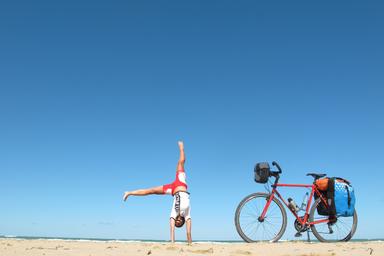 Sulla costa costa adriatica della Puglia, una ragazza vestita di rosa e bianco sta facendo una ruota sulla spiaggia. Accanto a lei la sua bicicletta