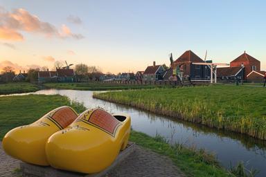 Posti su un piedistallo, degli zoccoli grandi gialli e sul retro il villaggio di Zaanse Schans, con le sue case pittoresche e tetti marroni, al tramonto