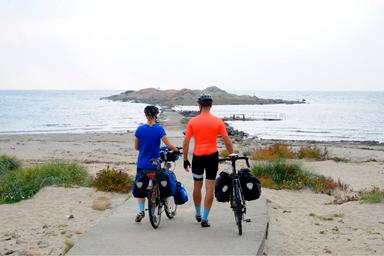 Due ciclisti, un uomo e una donna, guardano verso il mare svedese. Il cielo è aperto e all'orizzonte spicca un'isola